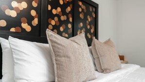 A bed with white bedding and beige pillows, a dark headboard with a bokeh light pattern, and a plain wall.