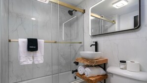 Ein modernes Badezimmer mit einer ein Glasfachwerk umschlossenen Dusche, einer weißen Toilette und einem Waschtisch mit einer Beckenwaschschale.