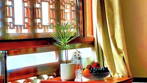 Una habitación con una mesa de madera, una planta en maceta, un frutero y una ventana con vista a un edificio.