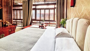 Una habitación tradicional con cama, muebles de madera y vistas al exterior a través de una ventana con cortinas estampadas.