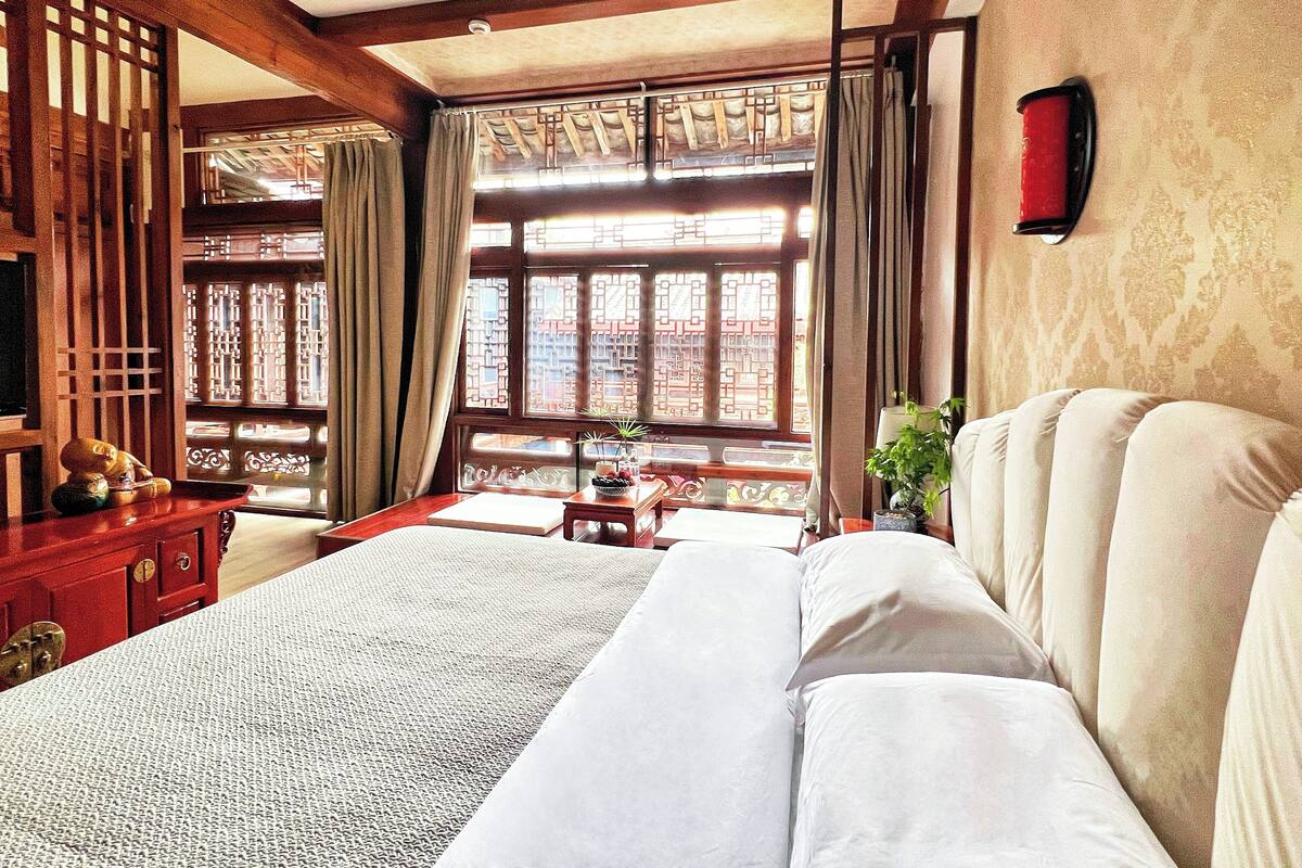 A traditional room with a bed, wooden furniture, and a view through a window with patterned curtains.