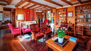 Un salón acogedor con vigas de madera, una pared roja y una estantería llena de libros y objetos decorativos.