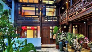 Un edificio tradicional con fachada de madera, varios balcones y un patio cuidado con plantas en macetas y suelo de baldosas.