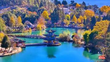 A serene lakeside park with traditional architecture, including a pagoda and pavilion, surrounded by autumn foliage.