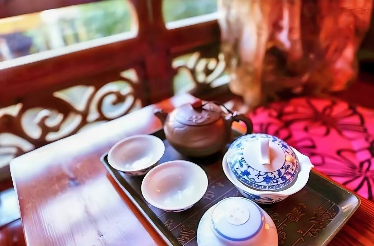 A tray with a teapot, two cups, and a small container on a table with a patterned tablecloth.
