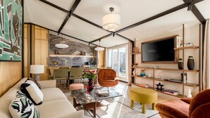 Een moderne woonkamer met een bank, fauteuil, salontafel en een aan de muur bevestigde televisie.