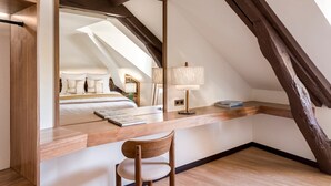 A bedroom with a sloped ceiling, a wooden desk, a chair, a bedside lamp, and a bed with pillows. - Merveil Signature Suite - Cyr II - Private terrace (Paris)