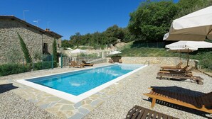 A swimming pool with stone tiles, surrounded by lounge chairs and umbrellas, set against a stone building and lush greenery. - Casa Minuccia - Vacation house in Chianti (Villa A Sesta)