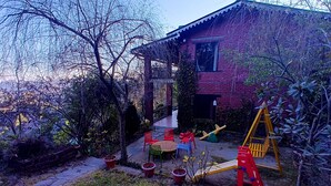 Een huis met een bakstenen gevel, een overdekte veranda en een schommel in de tuin.