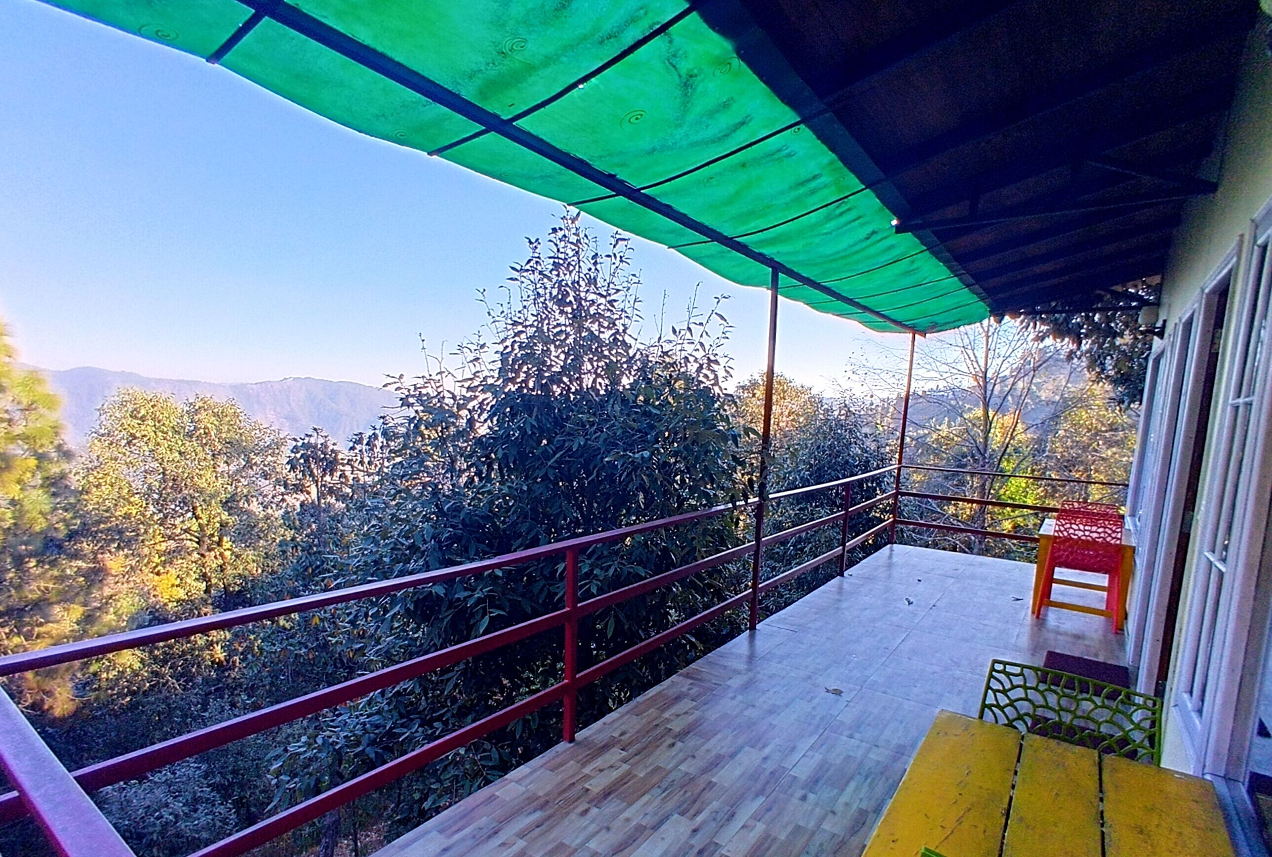 A balcony with a green canopy, a wooden floor, and a red railing.