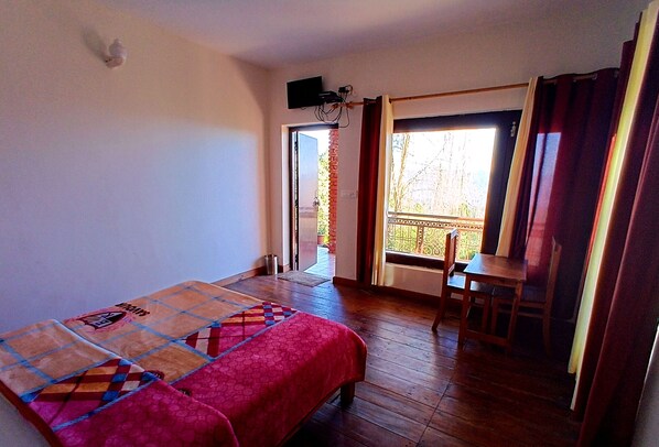Une pièce comprenant un lit, une table et une chaise. Il y a une fenêtre avec des rideaux et une porte donnant sur un espace extérieur.