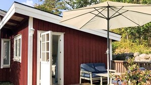 En träveranda med en enda blå stol och ett beige parasoll.