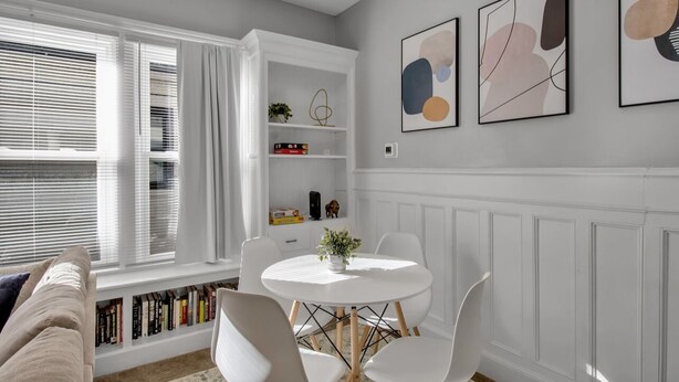 Ein modernes Wohnzimmer mit einem weißen runden Tisch, weißen Stühlen, einem Bücherregal und abstrakter Kunst an der Wand.