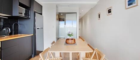 A modern kitchen with dark cabinetry, a wooden dining table, and a view into the living area.