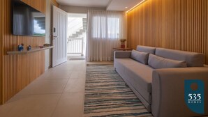 Una sala de estar moderna con un sofá, un televisor montado en la pared, un revestimiento de pared de madera y una escalera que conduce a un piso superior.