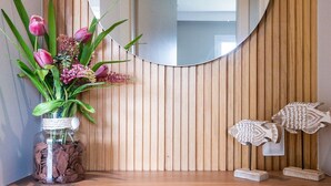 Pared de madera con un espejo redondo y un estante con un florero y objetos decorativos.