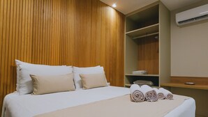 Una cama bien hecha con una colcha color beige y almohadas, un cabecero de listones de madera, un armario empotrado y un aire acondicionado de pared.