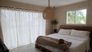 A bedroom with a wooden bed, white bedding, a woven hanging light, sheer curtains, a window with a view of palm trees, and a potted plant. - Waterfront House with Boat Dock (Tavernier)
