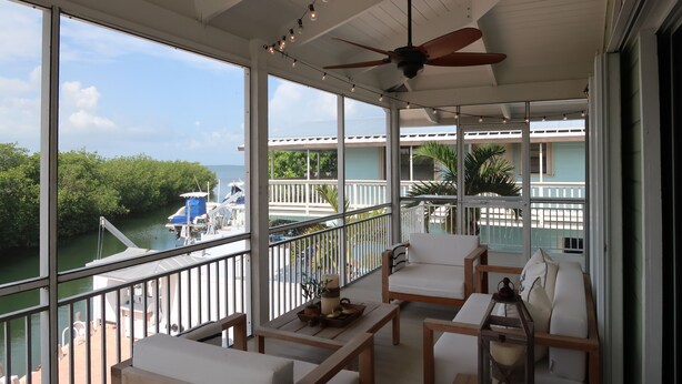 A balcony with white furniture, a ceiling fan, and a view of a boat and water. - Waterfront House with Boat Dock (Tavernier)