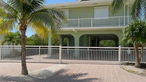 A two-story building with a balcony, surrounded by a white fence and palm trees. - Waterfront House with Boat Dock (Tavernier)