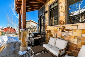 A covered patio with a stone wall, a grill, and outdoor furniture.