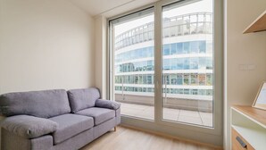 Un salon moderne avec un canapé gris, de grandes fenêtres et une vue sur un immeuble en verre.