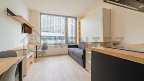 A modern, well-lit room with a large window, a desk, a sofa, and a TV mounted on the wall. - MyMozart City Center Residence: 702 (Prague)