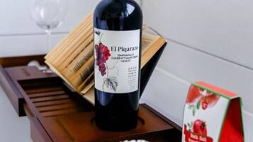 Una botella de vino El Picarazo sobre una bandeja de madera, junto con una copa de vino y una caja de zumo de granada.