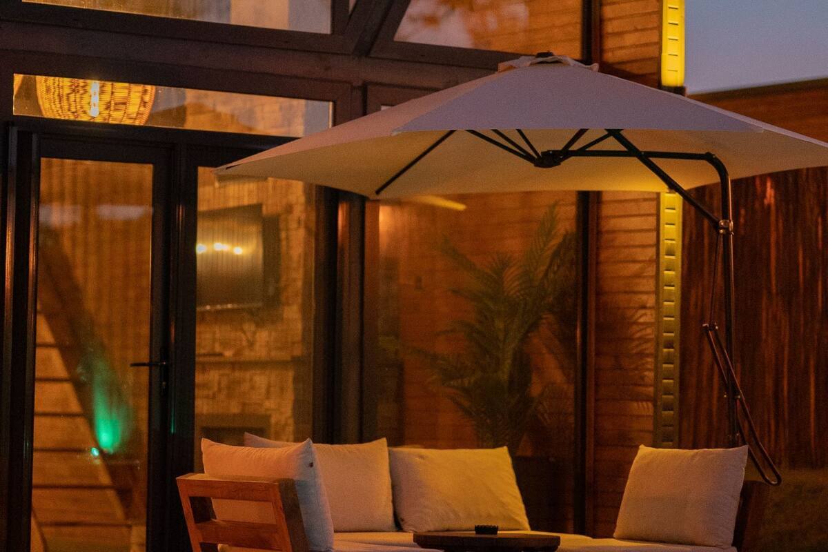 Un espace aménagé au bord de la piscine, avec une terrasse en bois, deux chaises longues et un grand parasol pour créer de l’ombre.