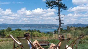 Trois personnes sont assises sur des chaises de jardin, face à un arbre et à un paysage pittoresque composé d’un lac et de montagnes.