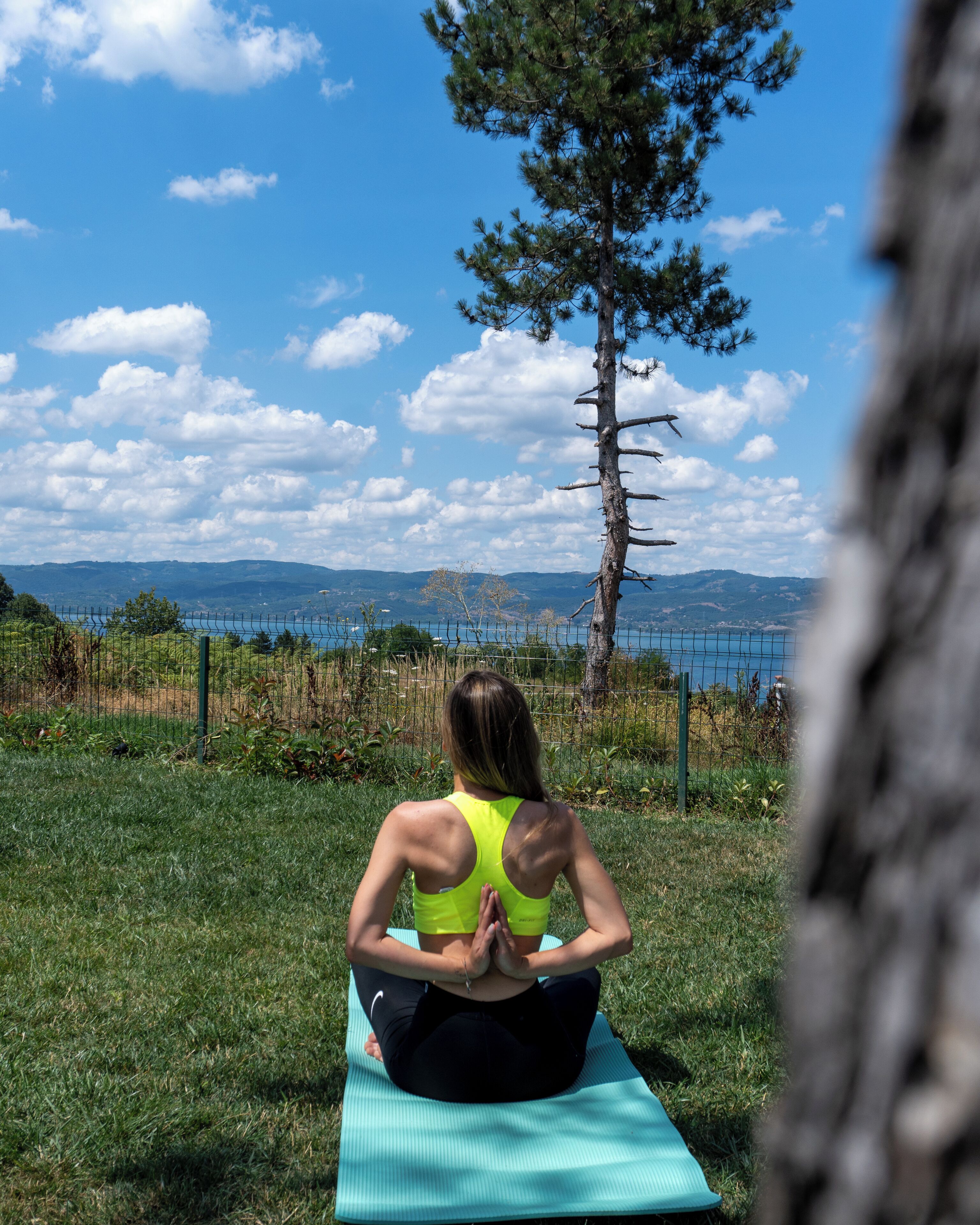 Iemand zit op een yogamatje buiten, met uitzicht op bergen en een hek op de achtergrond.