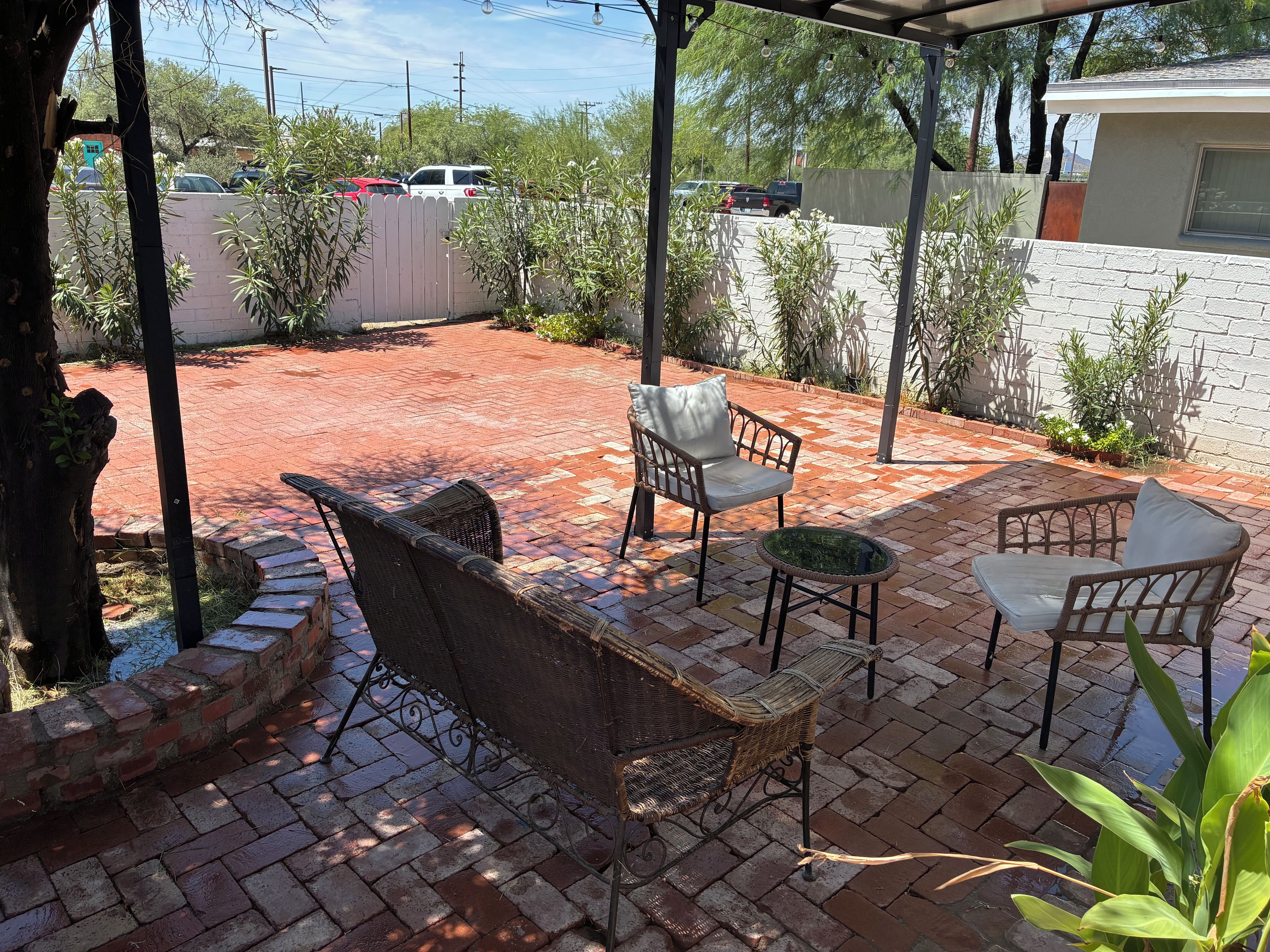 Un patio con suelo de ladrillo, mobiliario de mimbre y una pared blanca al fondo.