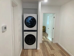 A laundry room with two stacked washing machines and a door leading to another room.