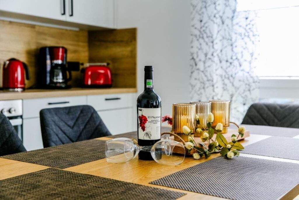 Una mesa de comedor con una botella de vino El Pijitaro, dos copas, y un arreglo decorativo de flores y velas.