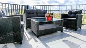 Ein Balkon mit Korbmöbeln, einem kleinen Tisch und einem roten Blumentopf.