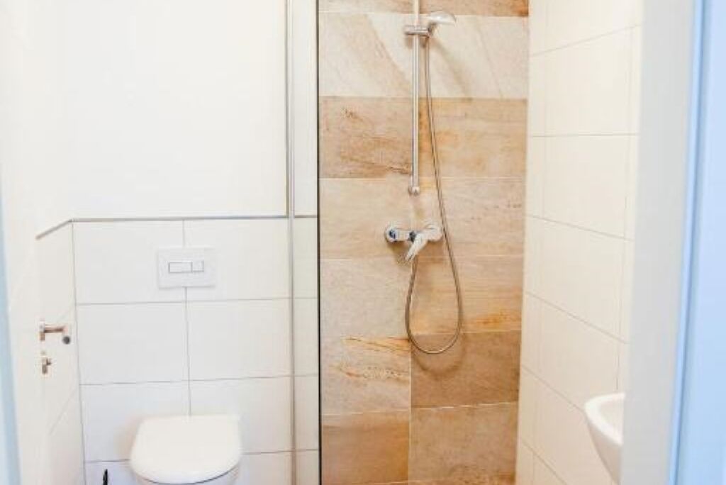 A small, compact bathroom with a white toilet, a shower with a handheld showerhead, and a wall-mounted sink.