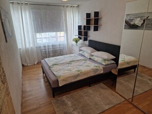 Une chambre à coucher avec un lit, une table de chevet, un miroir et une fenêtre avec des rideaux.