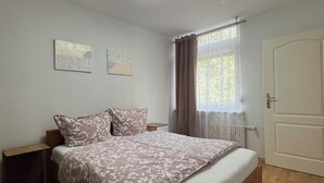 Ein Schlafzimmer mit einem Bett, zwei Nachttischen, einem Fenster mit Vorhängen und einer Tür.