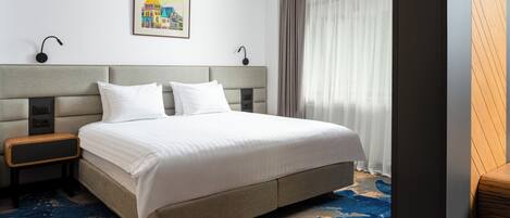 Una habitación de hotel con una cama grande, una mesita de noche, una lámpara de pared y un cuadro.