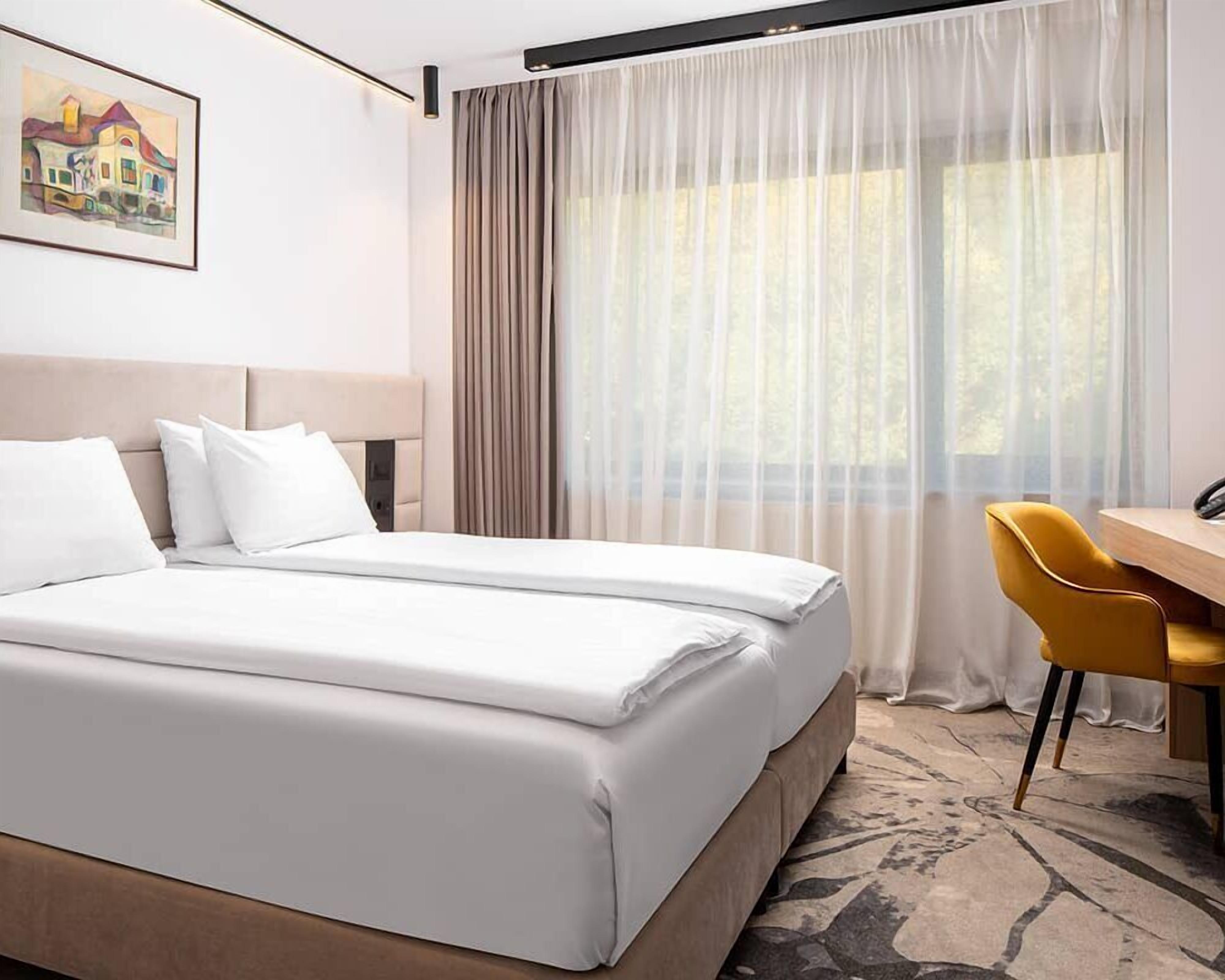 A hotel room with a bed, a desk, a chair, and a painting on the wall.