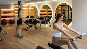 Een sportschool met trainingsapparatuur, een roeimachine en een persoon die de roeimachine gebruikt.