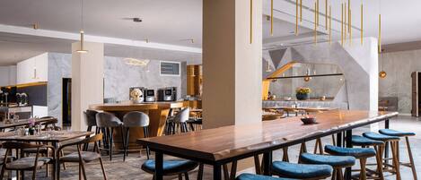 A modern kitchen with a marble backsplash, a wooden bar counter, and blue bar stools.