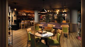 A restaurant with wooden flooring, green upholstered chairs, and pendant lighting.