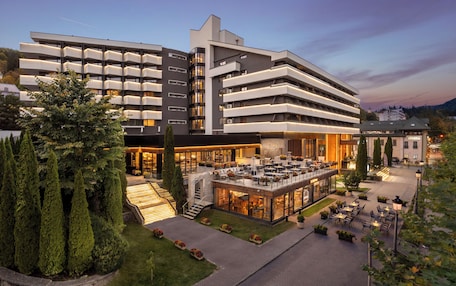 A modern hotel with multiple floors, outdoor seating area, and well-maintained landscaping.