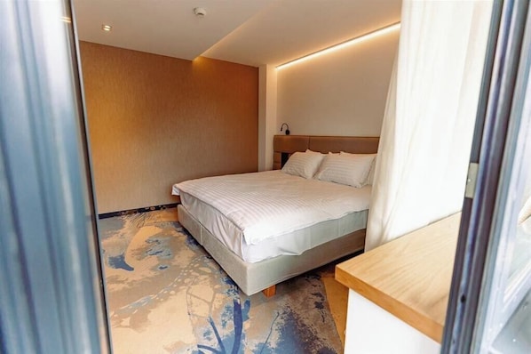 Habitación de hotel con una cama, cabecera de madera, mesita de noche y alfombra estampada.