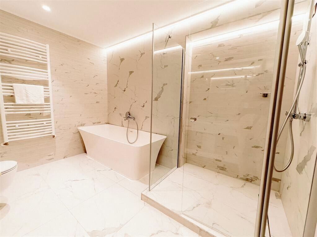 A modern bathroom with a freestanding bathtub, a glass-enclosed shower, and a marble-tiled floor.