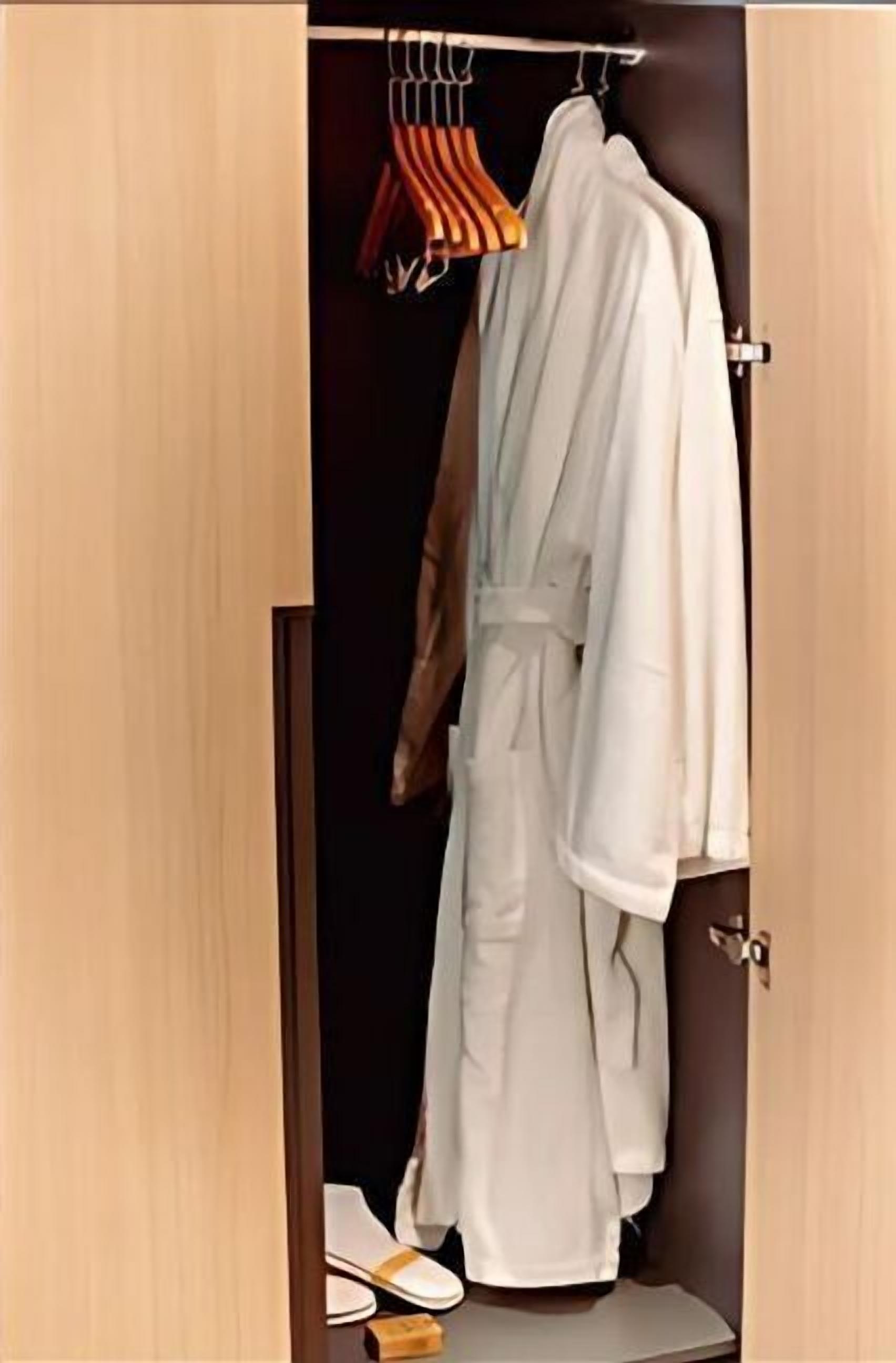 Un dressing où l’on peut entrer, avec une robe suspendue à un portant, une paire de chaussons sur le sol et une porte en bois.