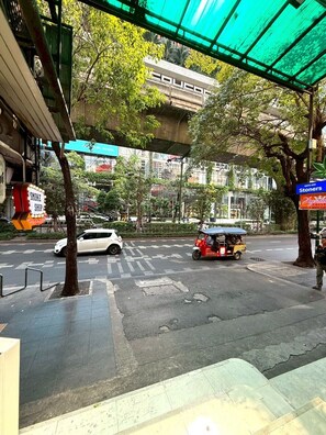 A street scene with a covered pedestrian area, a white car, a tuk-tuk, and a sign for a smoke shop.
