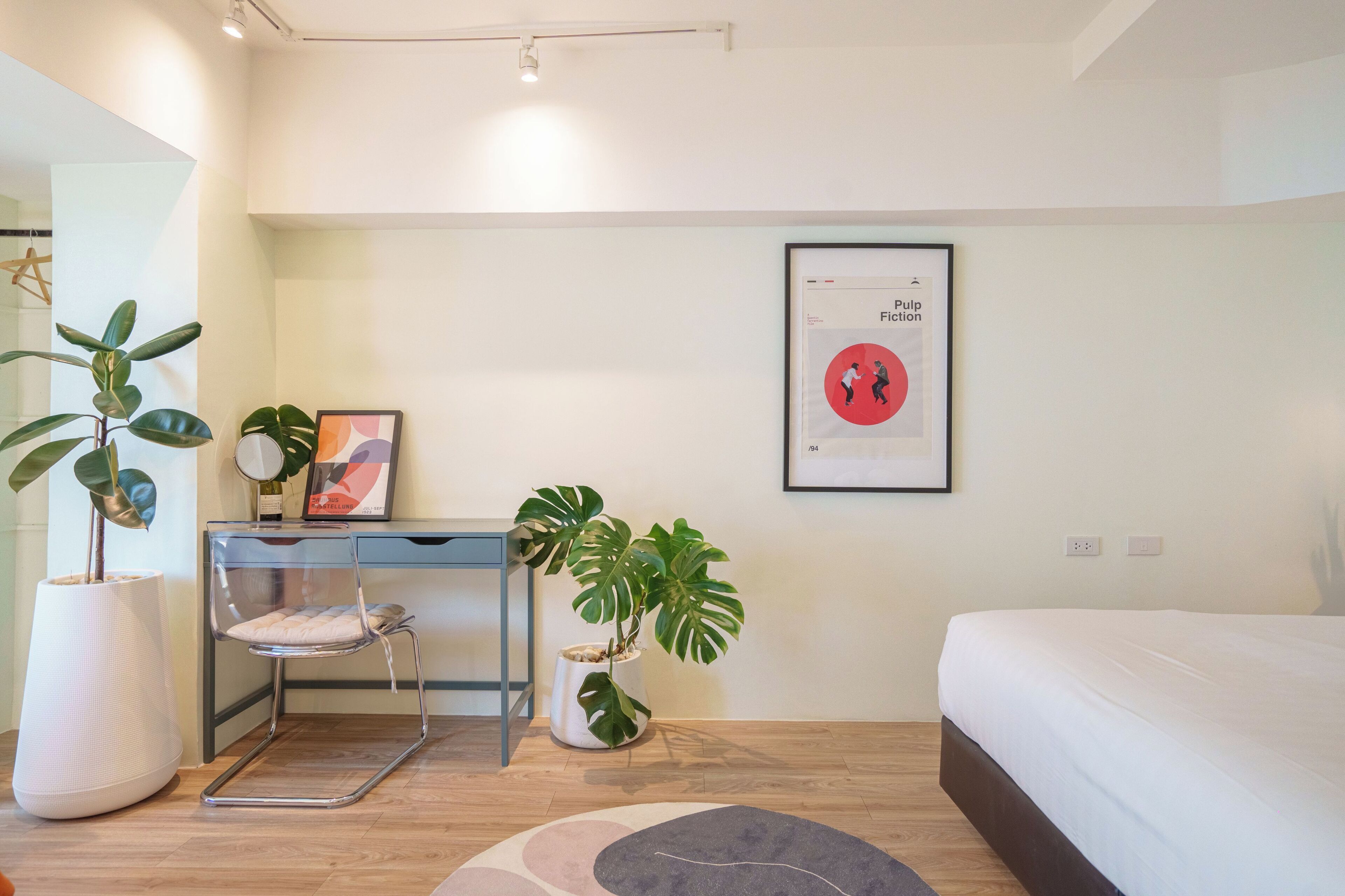 A modern bedroom with a bed, a desk, and two potted plants.