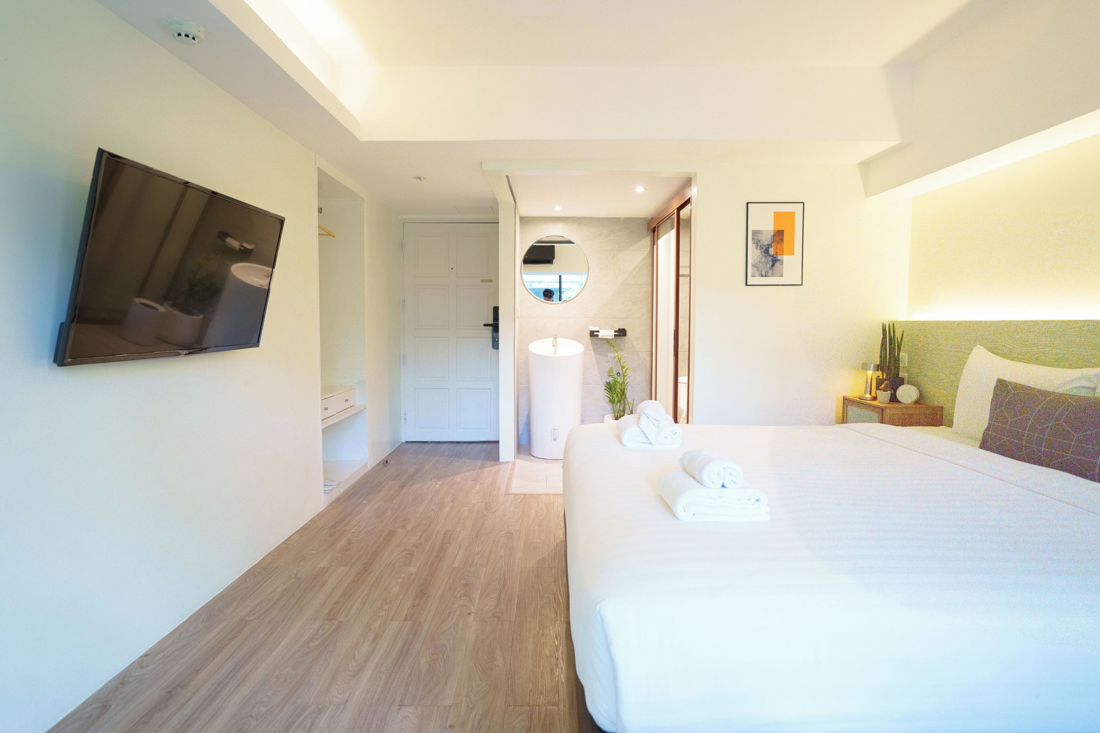 A hotel room with a large bed, a television mounted on the wall, a bedside table with a lamp, and a mirror above the sink.